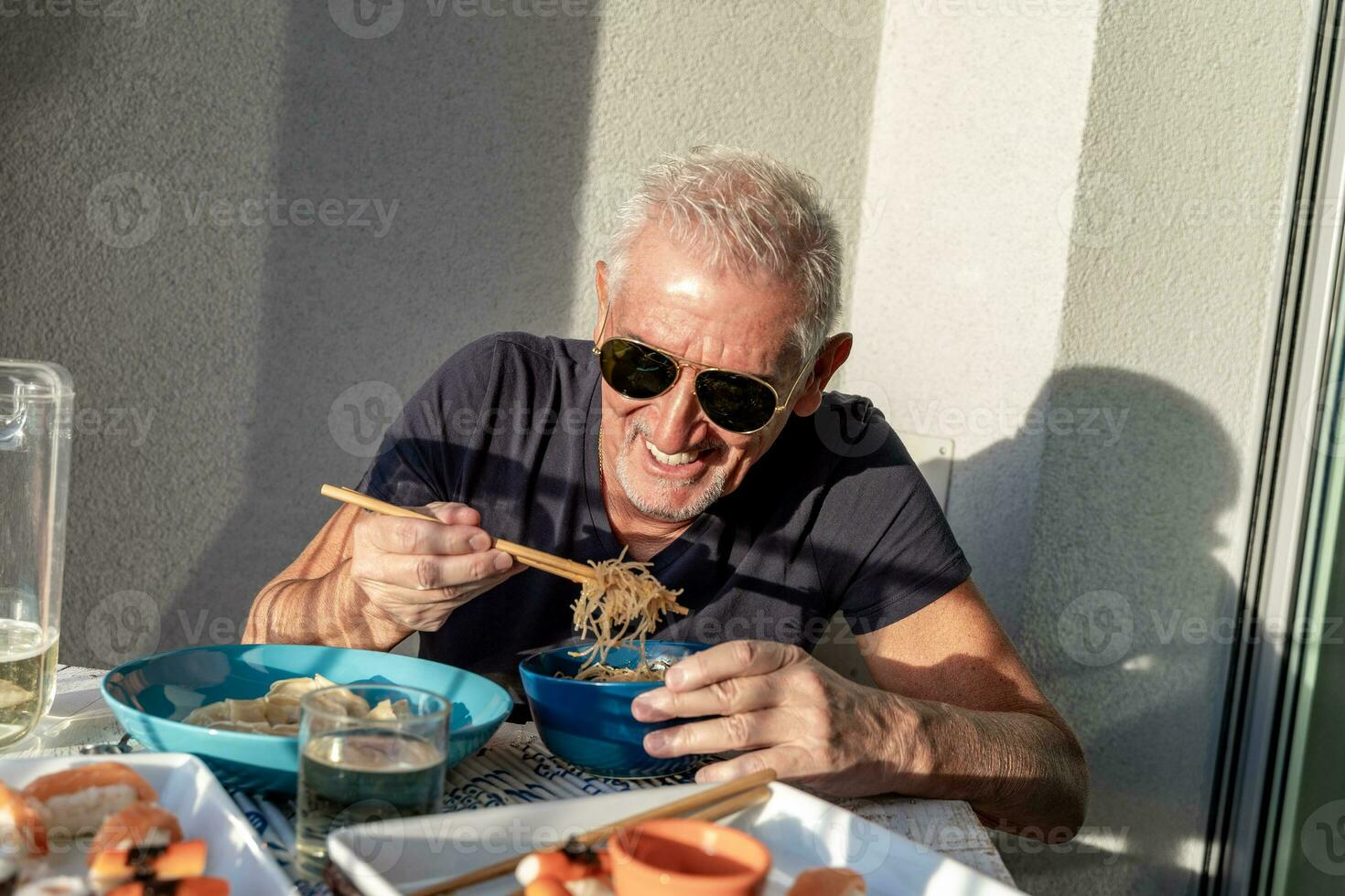 attraente di mezza età uomo avere divertimento mentre mangiare seduta a un' tavolo di cui Cinese prendere lontano cibo foto