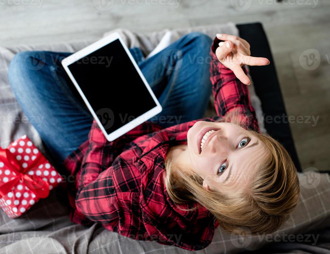 giovane donna bionda che lavora su tablet seduta sul divano, vista dall'alto foto