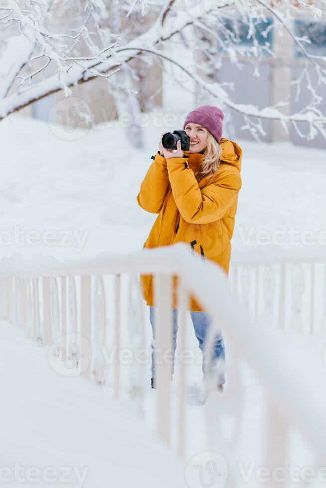 bellissimo ragazza nel un' giallo giacca fotografo prende immagini di neve nel un' inverno parco foto