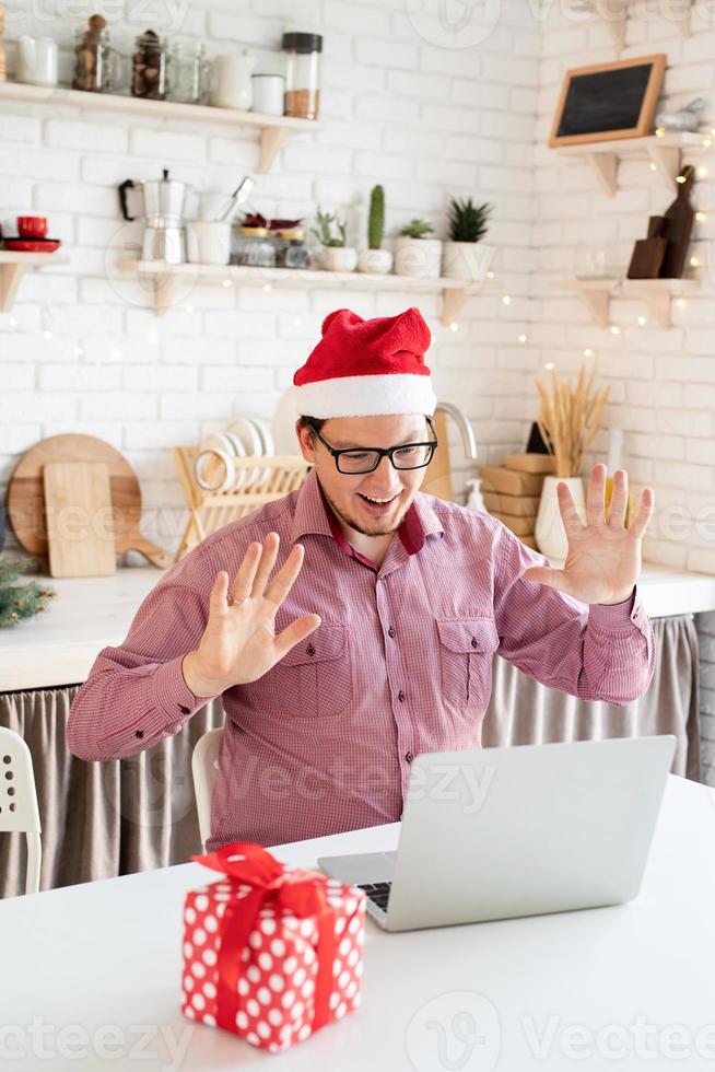 uomo con cappello da Babbo Natale saluta i suoi amici in video chat o chiama sul laptop foto