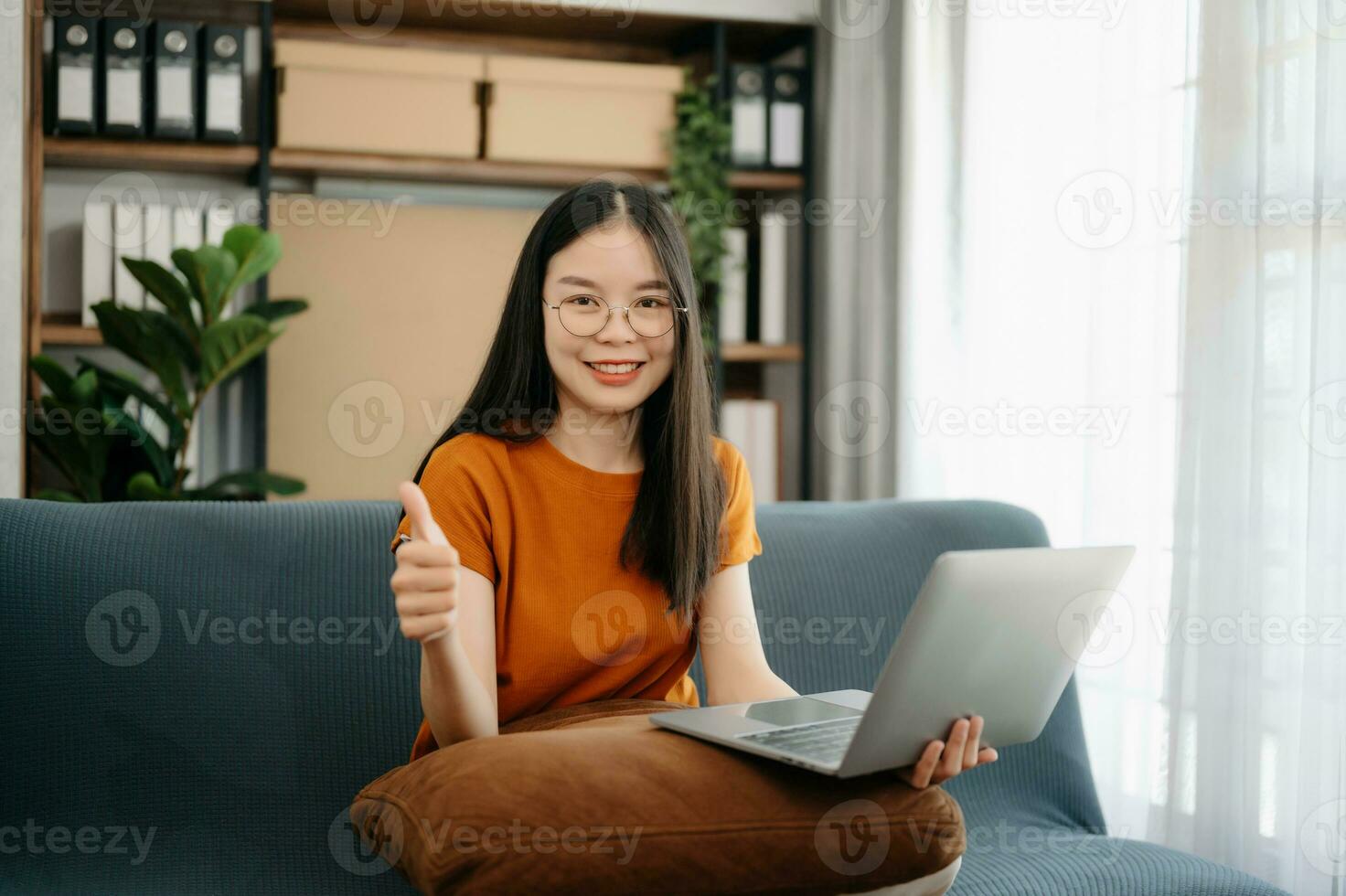 femmina studenti Nota a partire dal il libri a il asiatico ragazza biblioteca seduta a il divano utilizzando il computer portatile computer e tavoletta per ricerca un in linea informazioni. foto