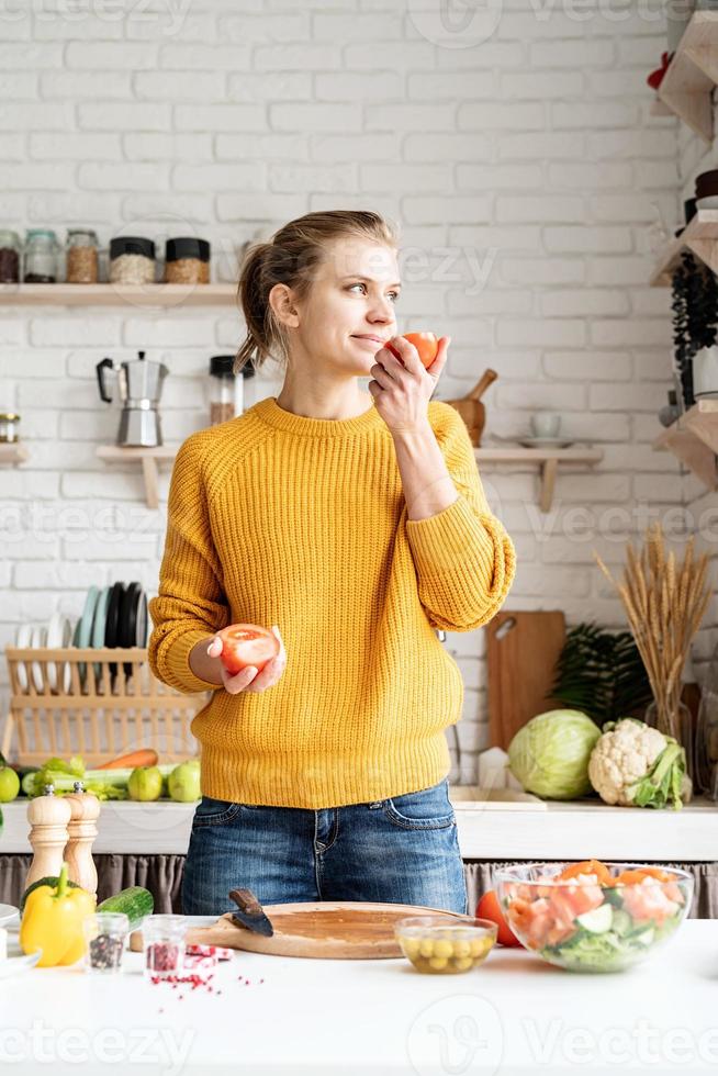 donna che odora un pomodoro e prepara l'insalata in cucina foto