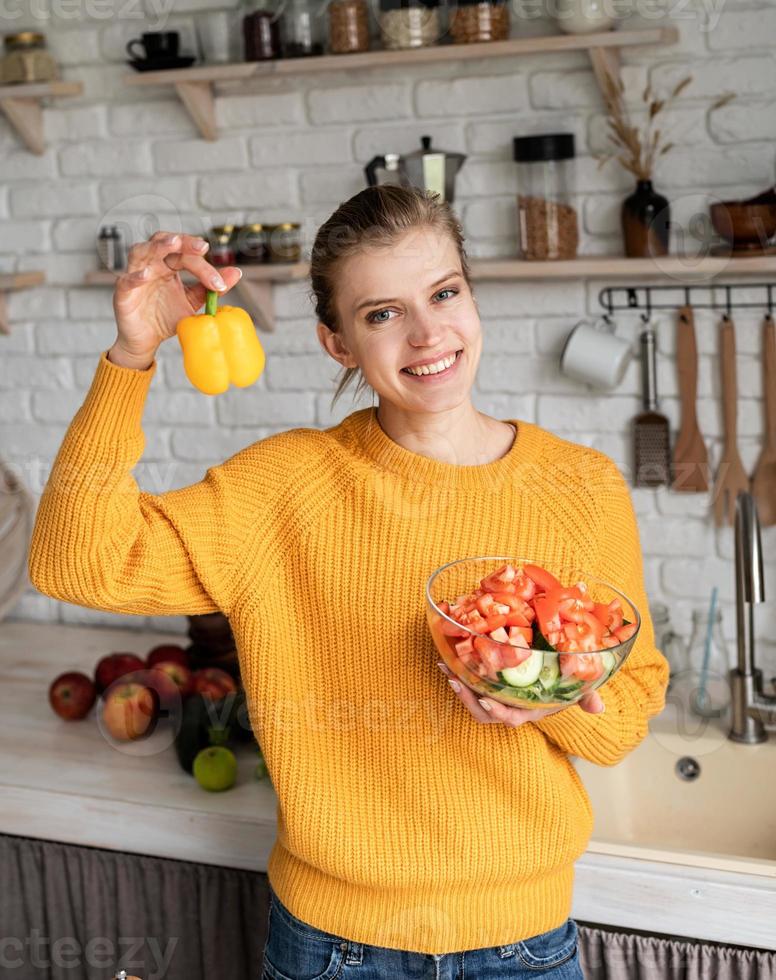 fare insalata di verdure tenendo un peperone giallo in cucina foto