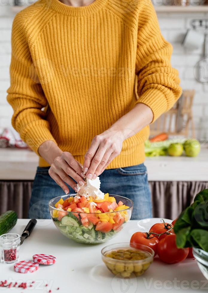 mani femminili che preparano l'insalata tagliando il formaggio feta in cucina foto