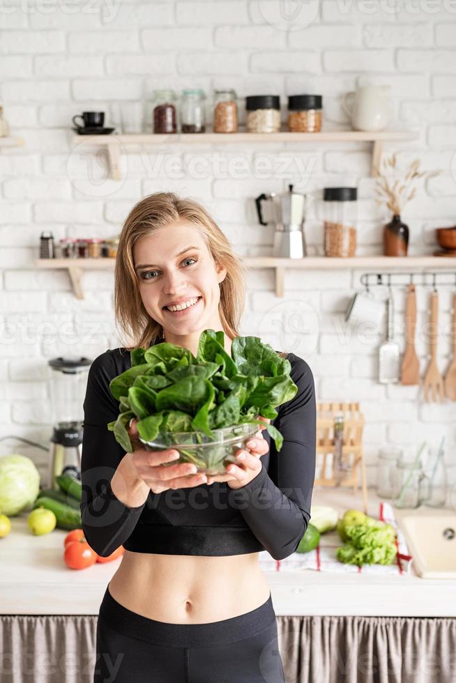 donna sorridente che tiene una ciotola di spinaci freschi in cucina foto