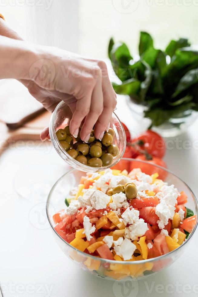 mani femminili che preparano insalata greca aggiungendo olive alla ciotola foto