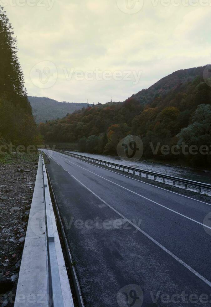 strada nel autunno foresta a tramonto nel carpazi montagne, Ucraina. bellissimo montagna carreggiata con arancia alberi e alto rocce. paesaggio con vuoto autostrada attraverso il boschi nel autunno foto