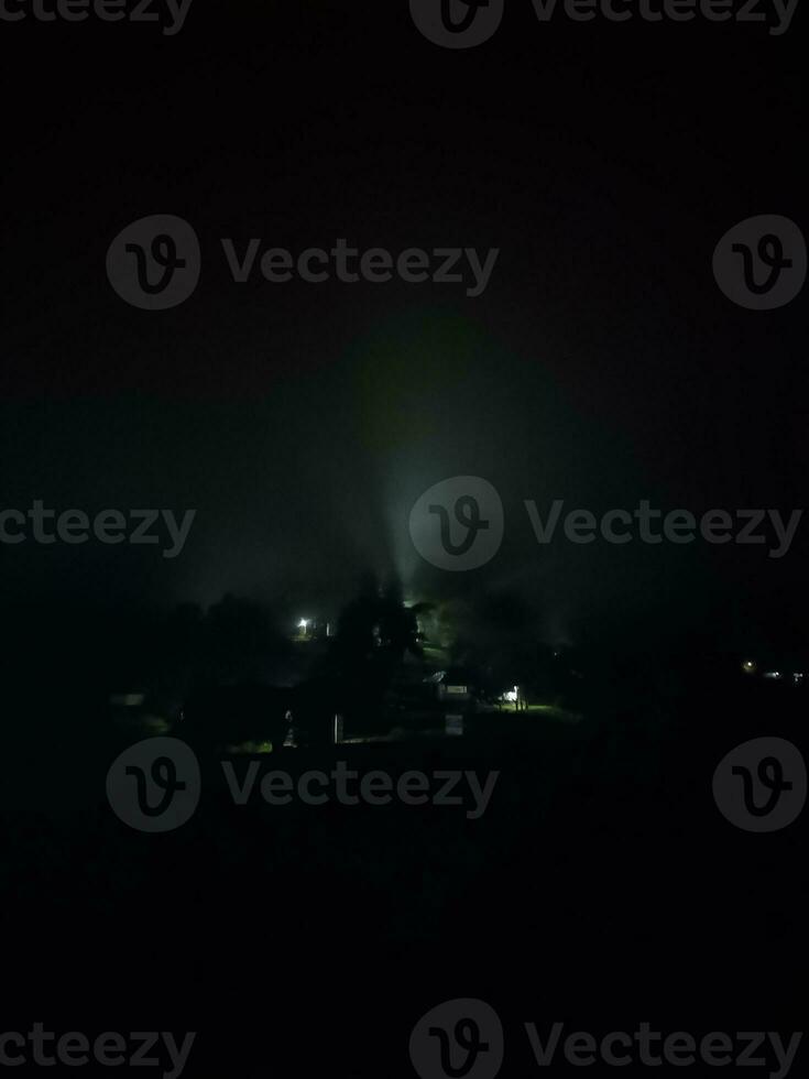 abete alberi su prato fra pendii con conifera foresta nel nebbia sotto il blu cielo a notte. spaventoso campagna scenario nel pieno Luna leggero foto