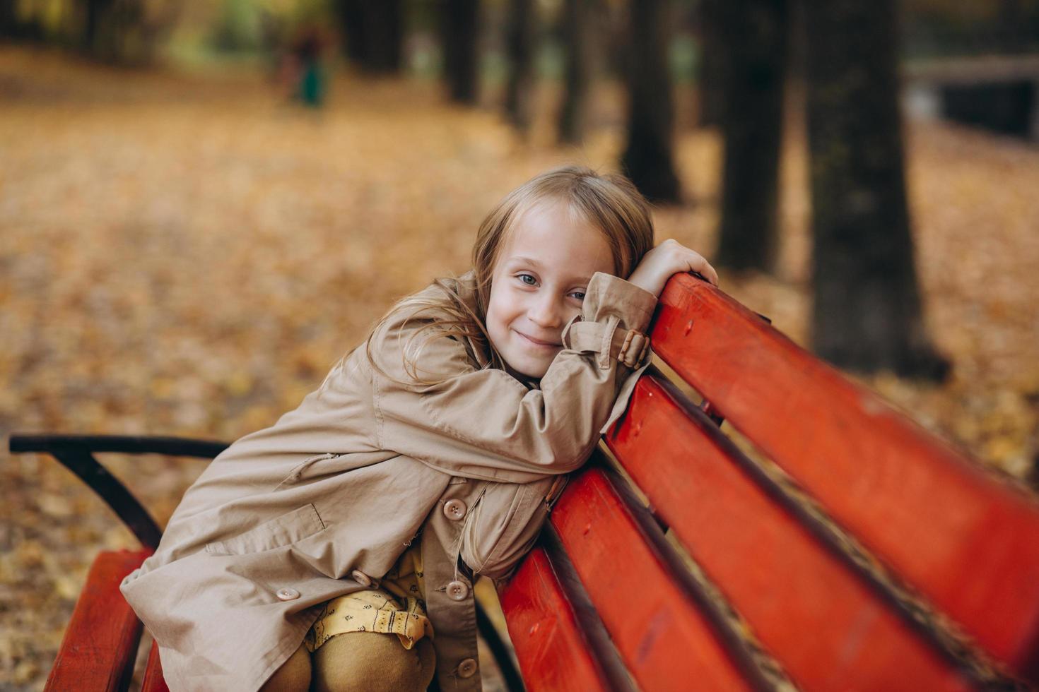 una bambina con un vestito giallo e un cappotto beige cammina nel parco autunnale foto