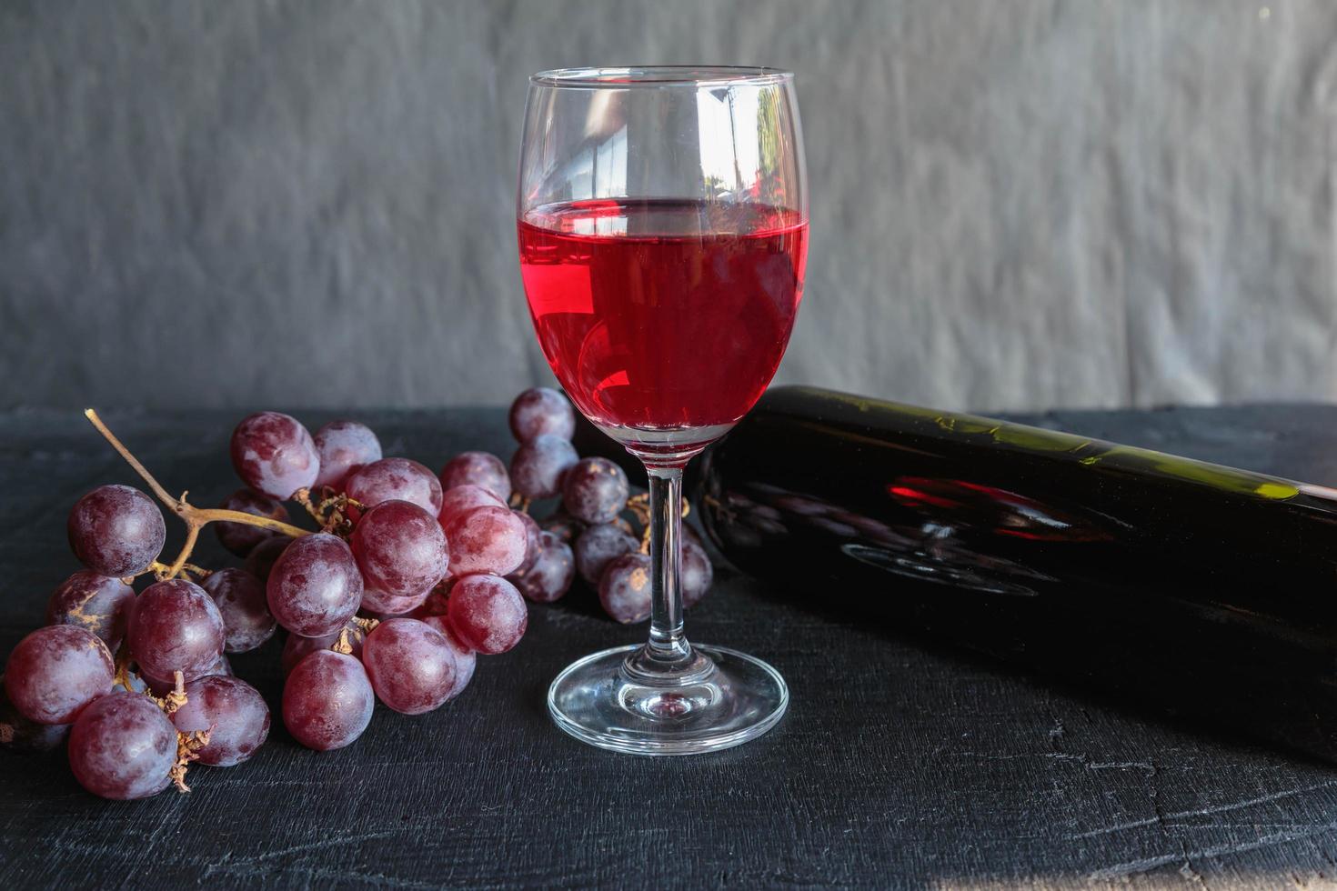 vino rosso e bottiglia di vino con uva su sfondo nero foto