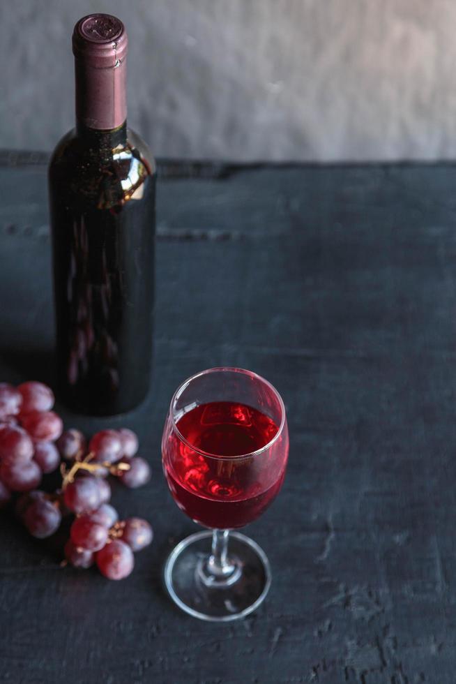 vino rosso e bottiglia di vino con uva su sfondo nero foto