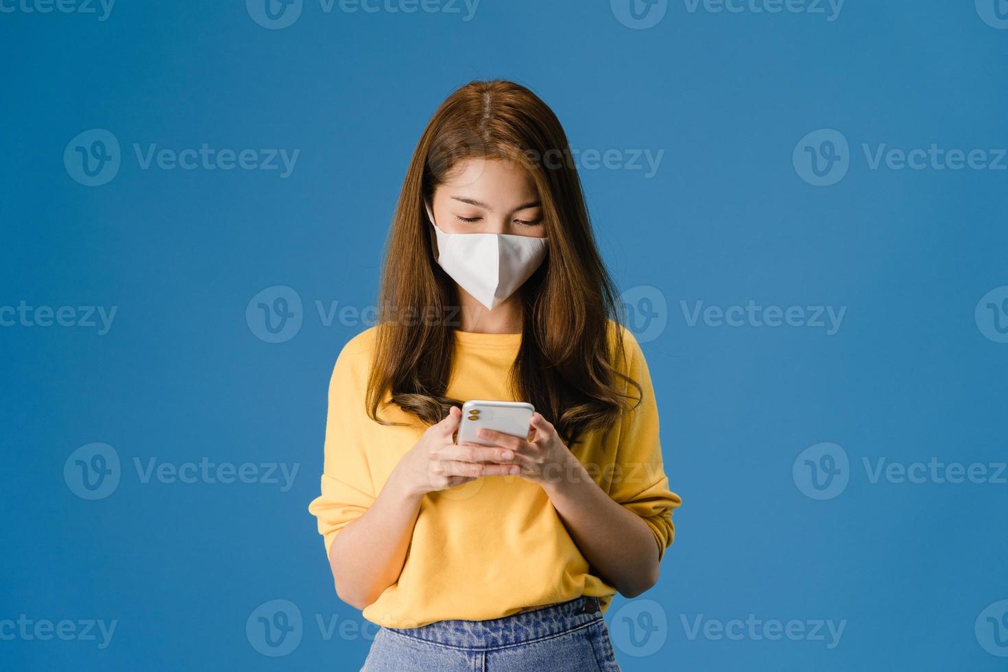 la giovane ragazza asiatica indossa la maschera facciale utilizzando il telefono cellulare su sfondo blu. foto