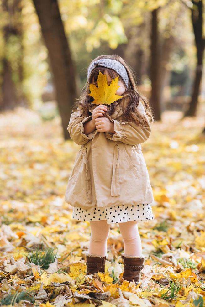 bambina felice che tiene una foglia d'acero gialla nel parco autunnale foto