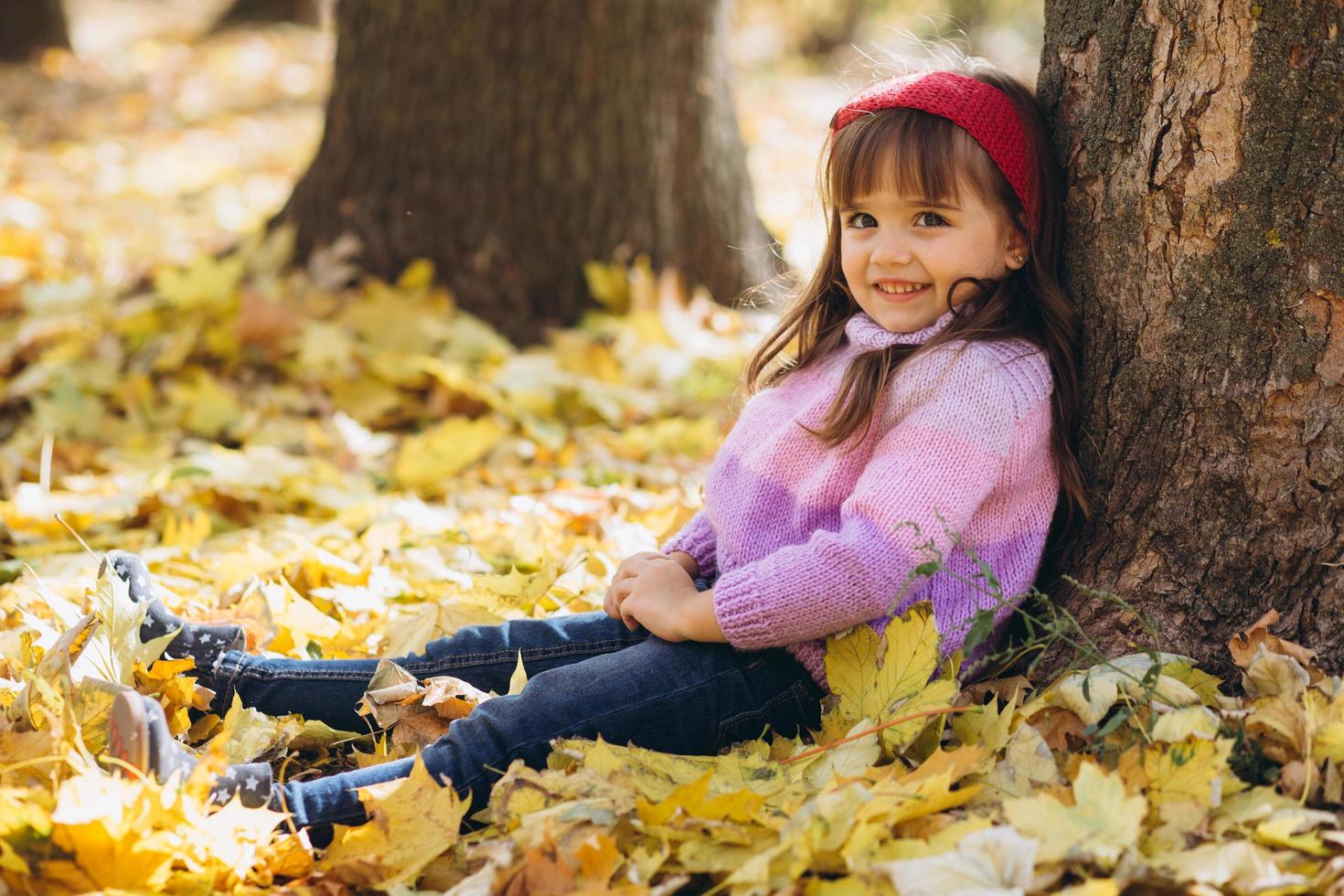 bambina seduta tra le foglie autunnali gialle nel parco foto