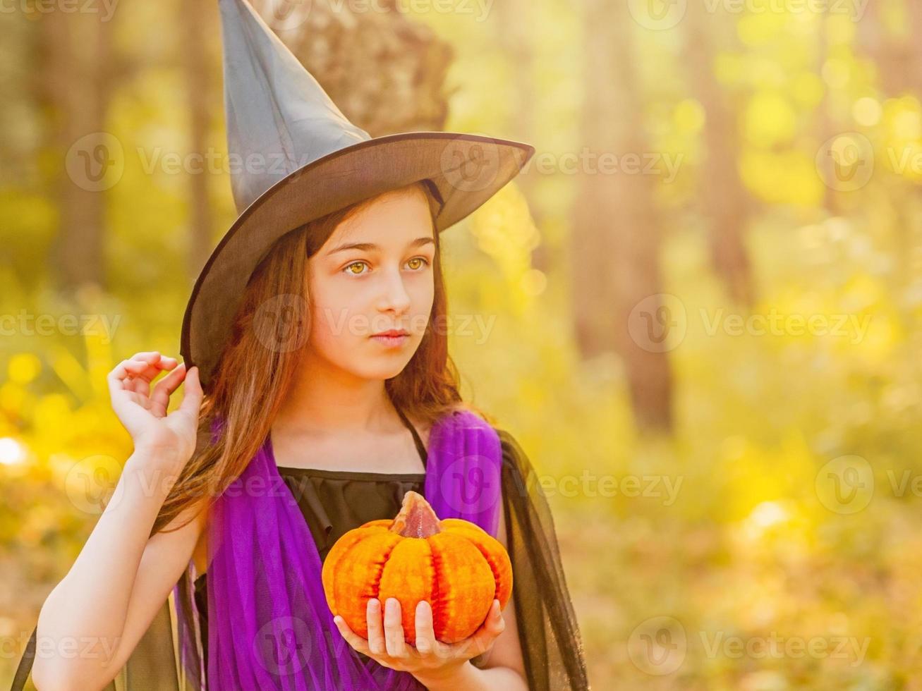 ragazza in un costume di halloween nella foresta con una zucca foto