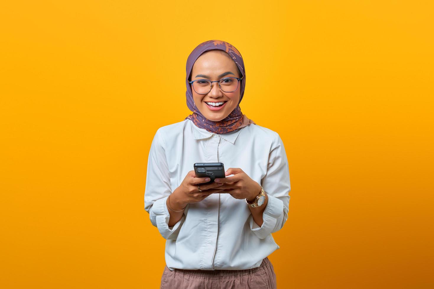 donna asiatica sorridente che utilizza il telefono cellulare e che guarda l'obbiettivo foto