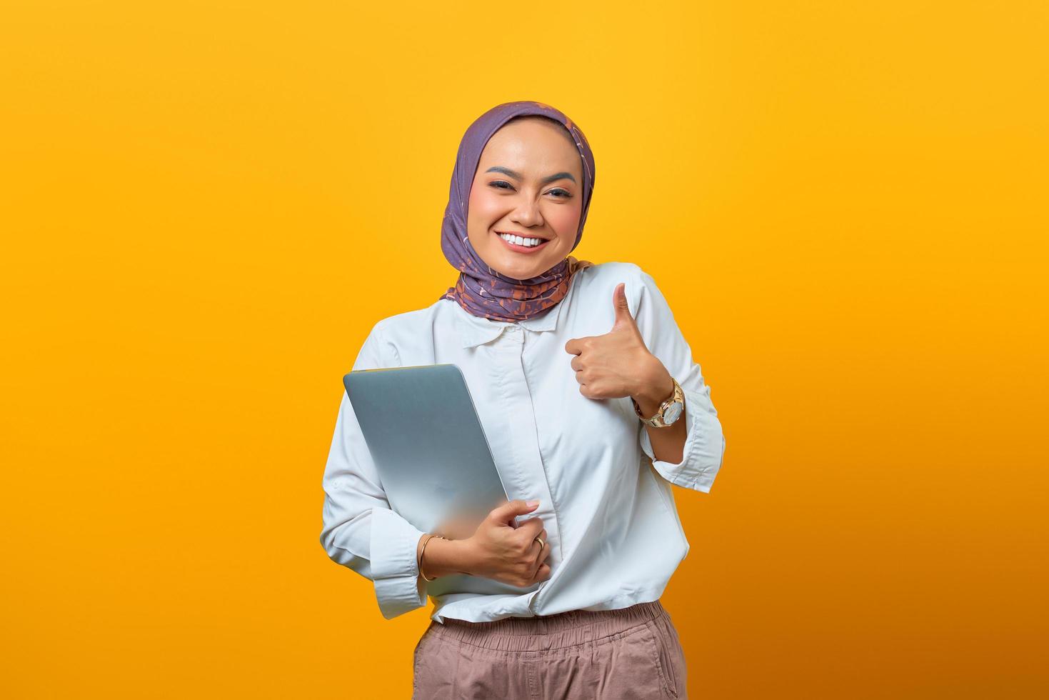 donna asiatica che tiene il computer portatile che sorride e che mostra i pollici in su segno foto