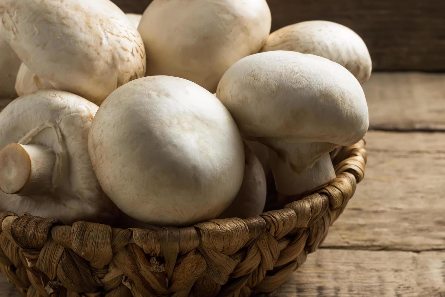 funghi champignon in un cesto di vimini su uno sfondo di legno foto