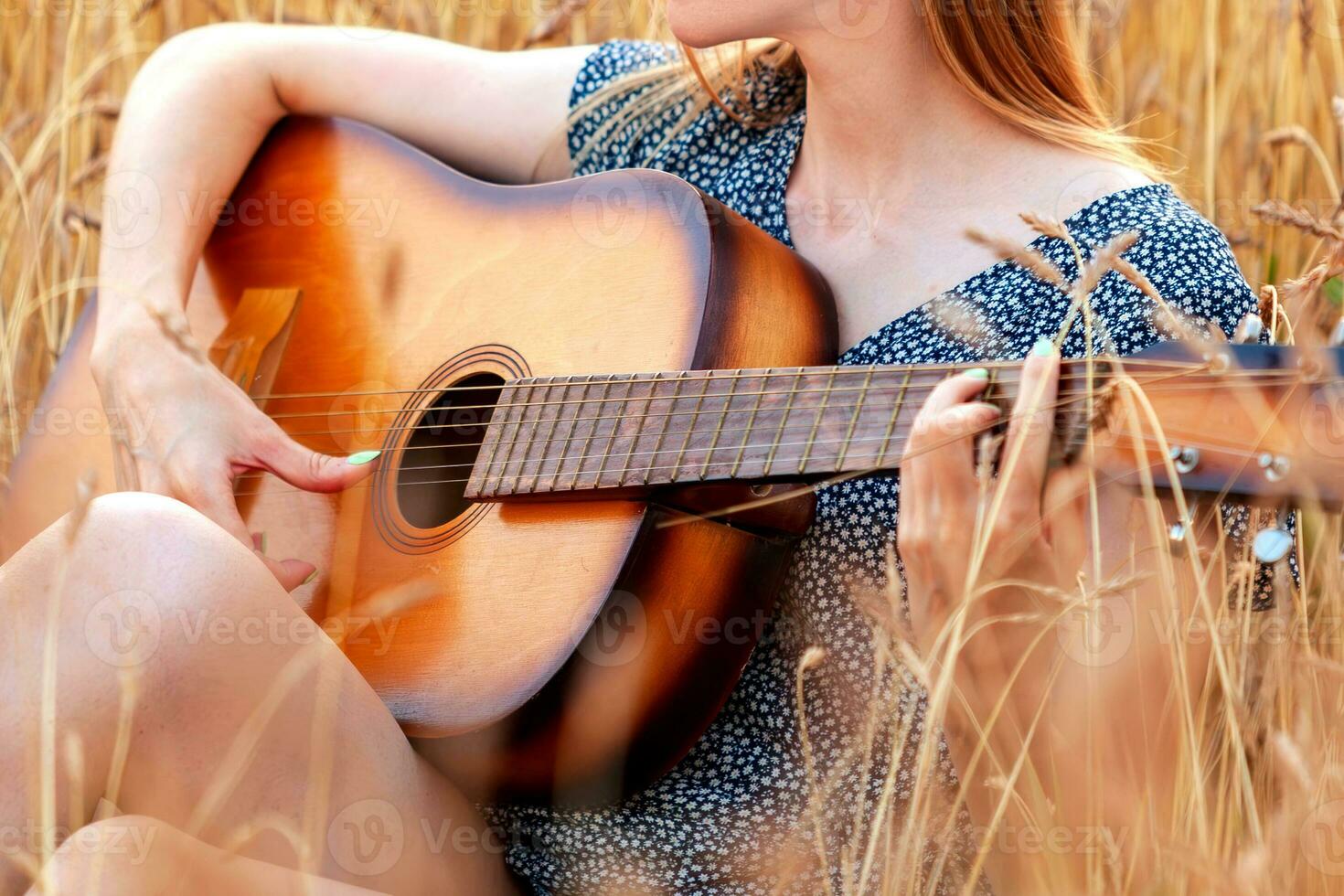 bellissimo giovane donna seduta nel Grano campo e giocando acustico chitarra. foto