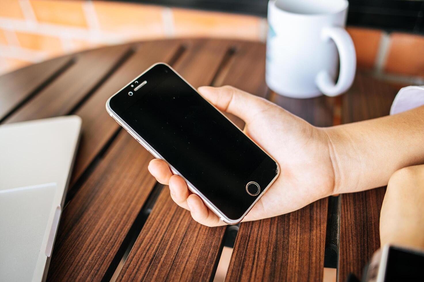 smartphone a portata di mano con tavolo e tazza foto