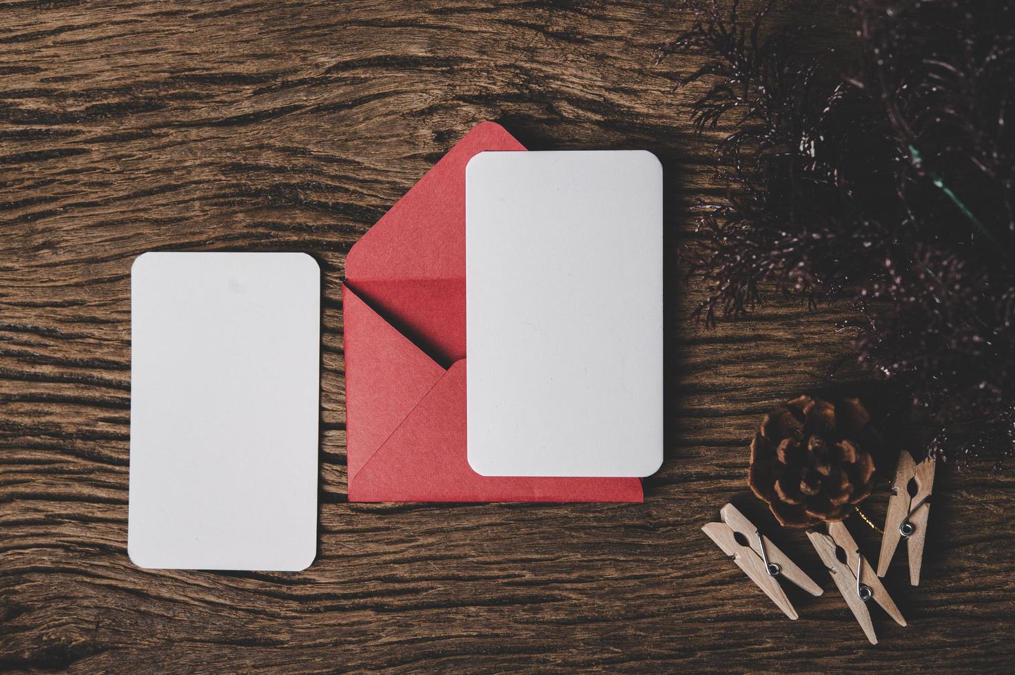 due carte vuote con busta rossa e molletta sono posizionate su legno. foto