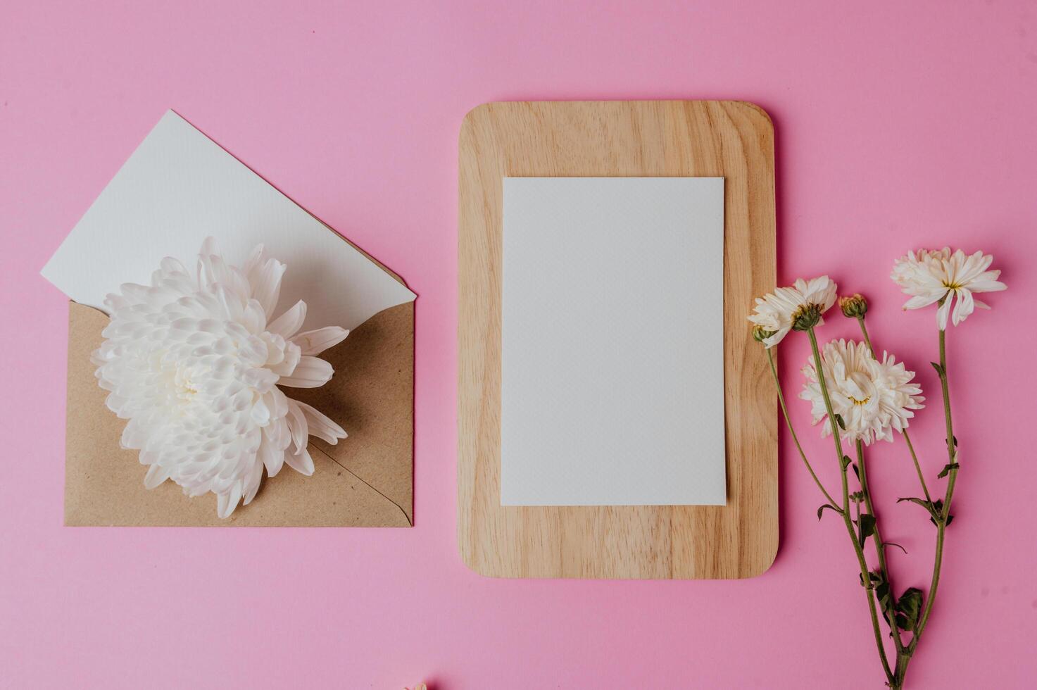 busta marrone, fiore e carta bianca su piatto di legno con rosa foto