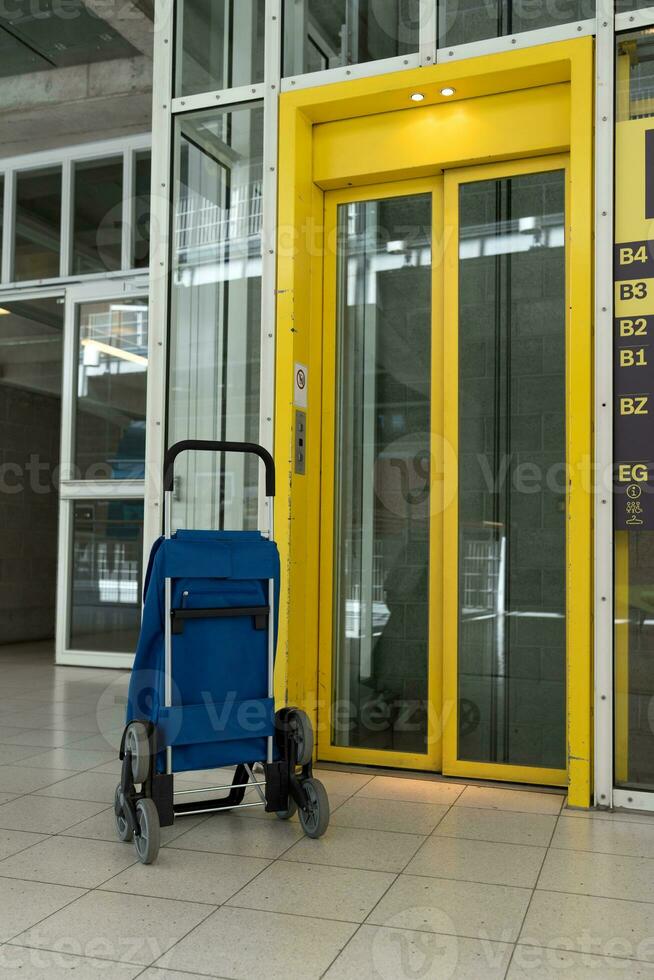 un' blu Borsa su ruote sta Il prossimo per un' giallo ascensore. blu-giallo. shopping carrelli. foto