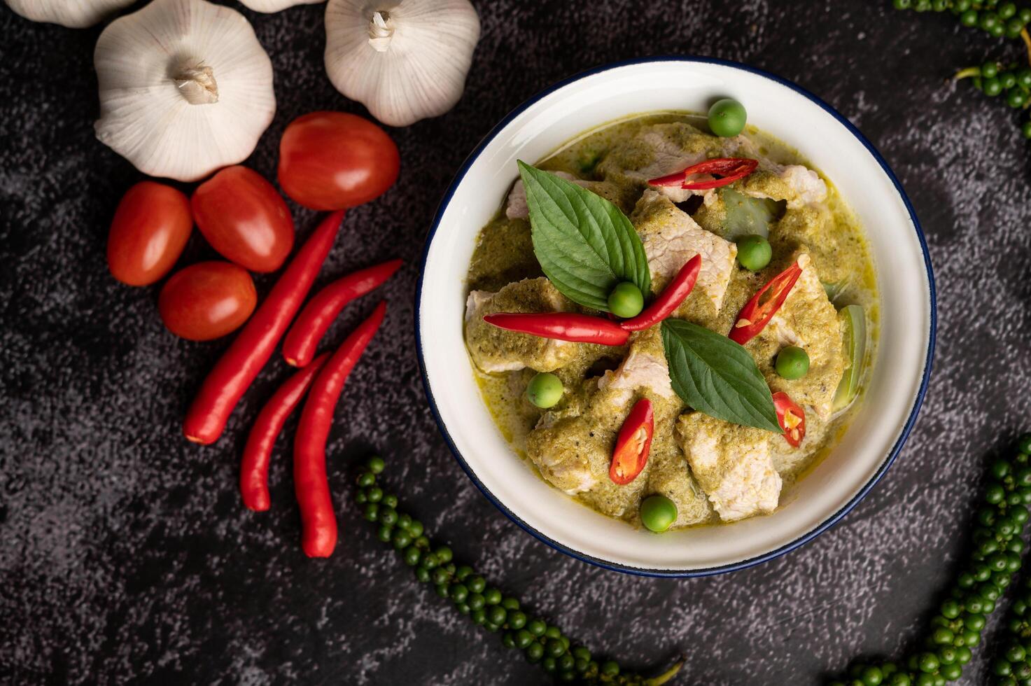 maiale al curry verde in una ciotola bianca con spezie su un cemento nero foto