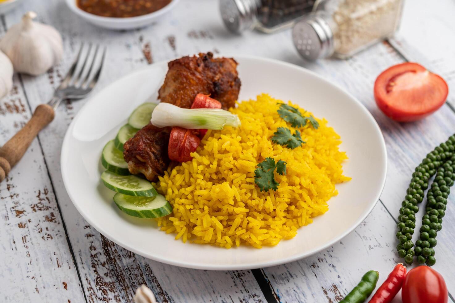 biryani di pollo in un piatto con spezie su un pavimento di legno bianco foto