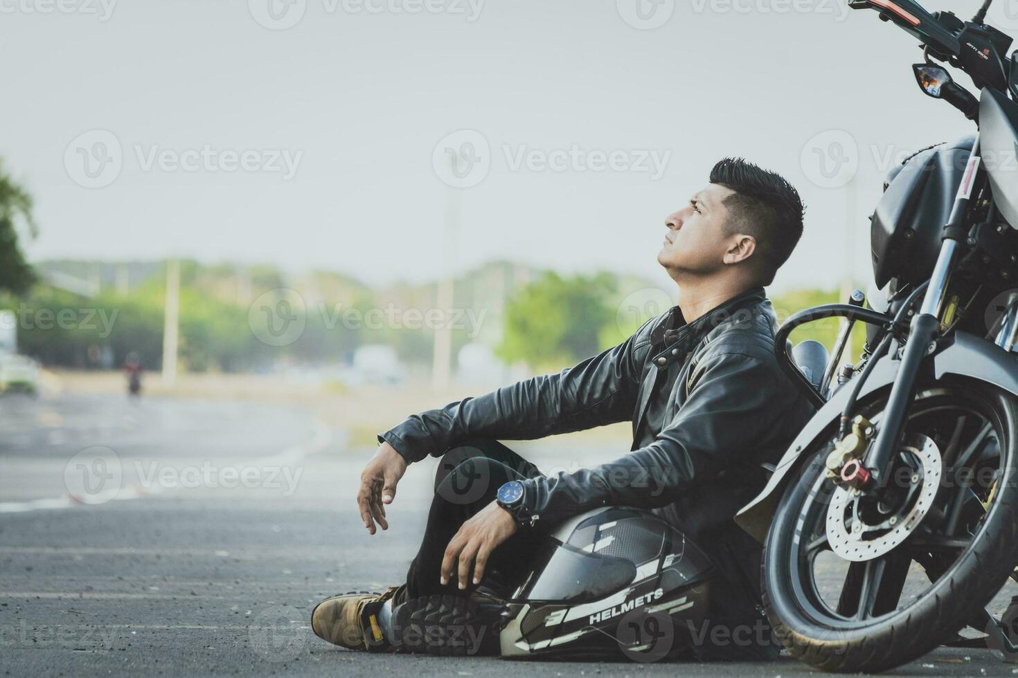 maschio motociclista seduta e pendente su il suo motociclo su il asfalto. motociclista seduta Il prossimo per il suo motociclo su il strada foto