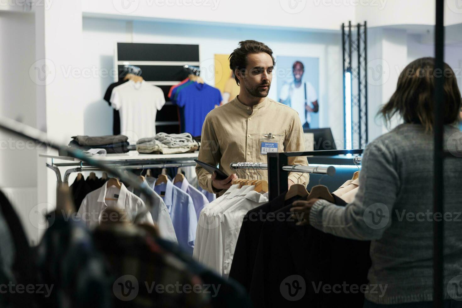 shopping centro dipendente utilizzando tavoletta per gestire abbigliamento azione mentre parlando con collaboratore. capi di abbigliamento memorizzare caucasico uomo lavoratore l'esame indumento su sito web mentre Lavorando nel boutique foto