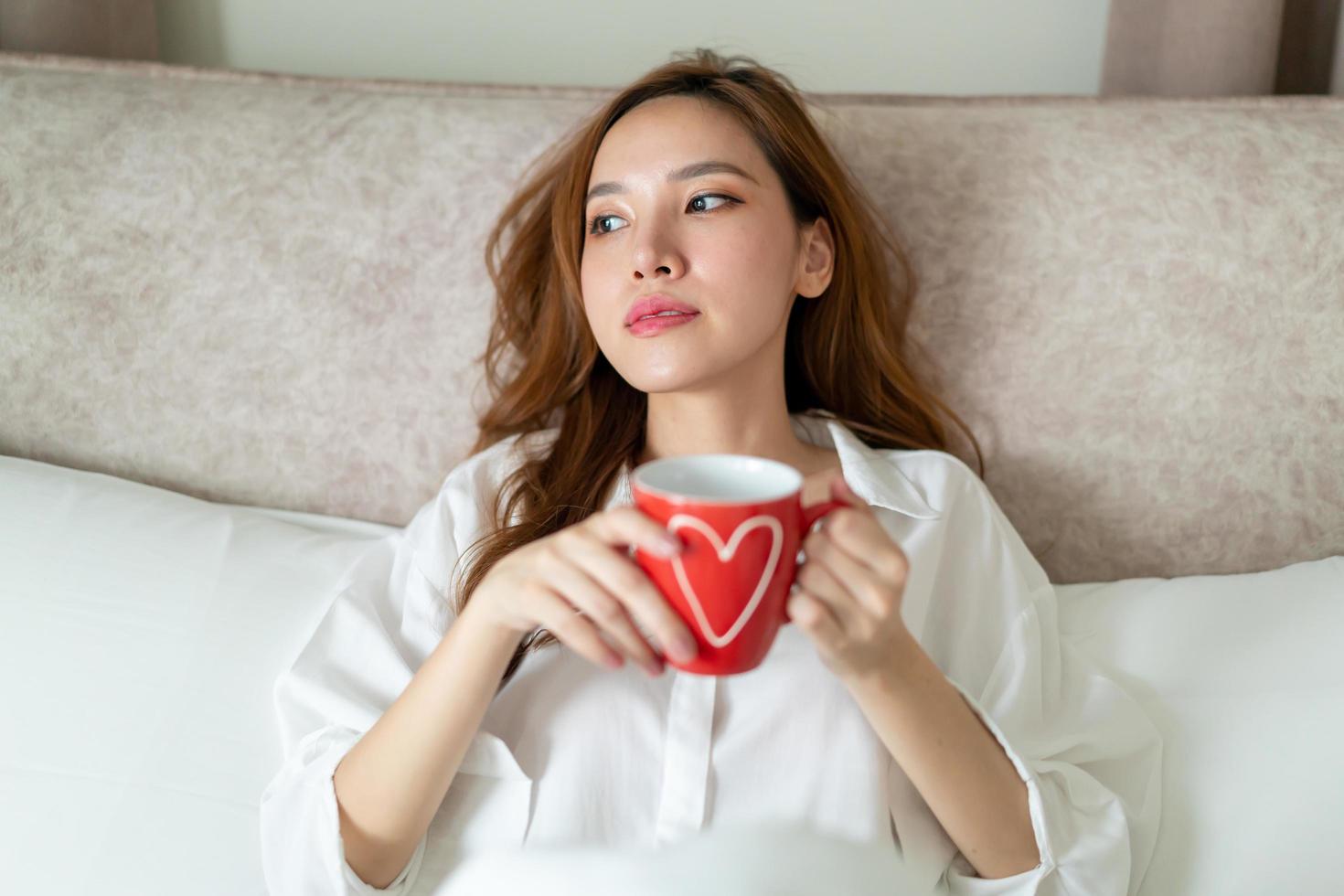 ritratto bella donna sveglia e tenendo tazza di caffè o tazza sul letto foto