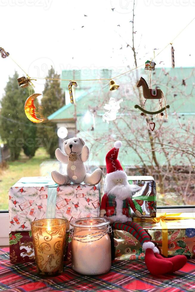 giocattolo gnomo con orsacchiotto orso seduta su Natale i regali con candele nel bicchiere candelieri vicino il finestra nel un' rurale Casa, verticale foto