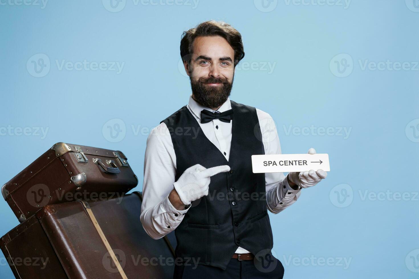 sorridente fattorino pose con terme cartello per guida visitatori e presente diverso Hotel le zone, turismo industria. allegro professionale portiere Tenere indicatore come direzione per rilassamento la zona. foto