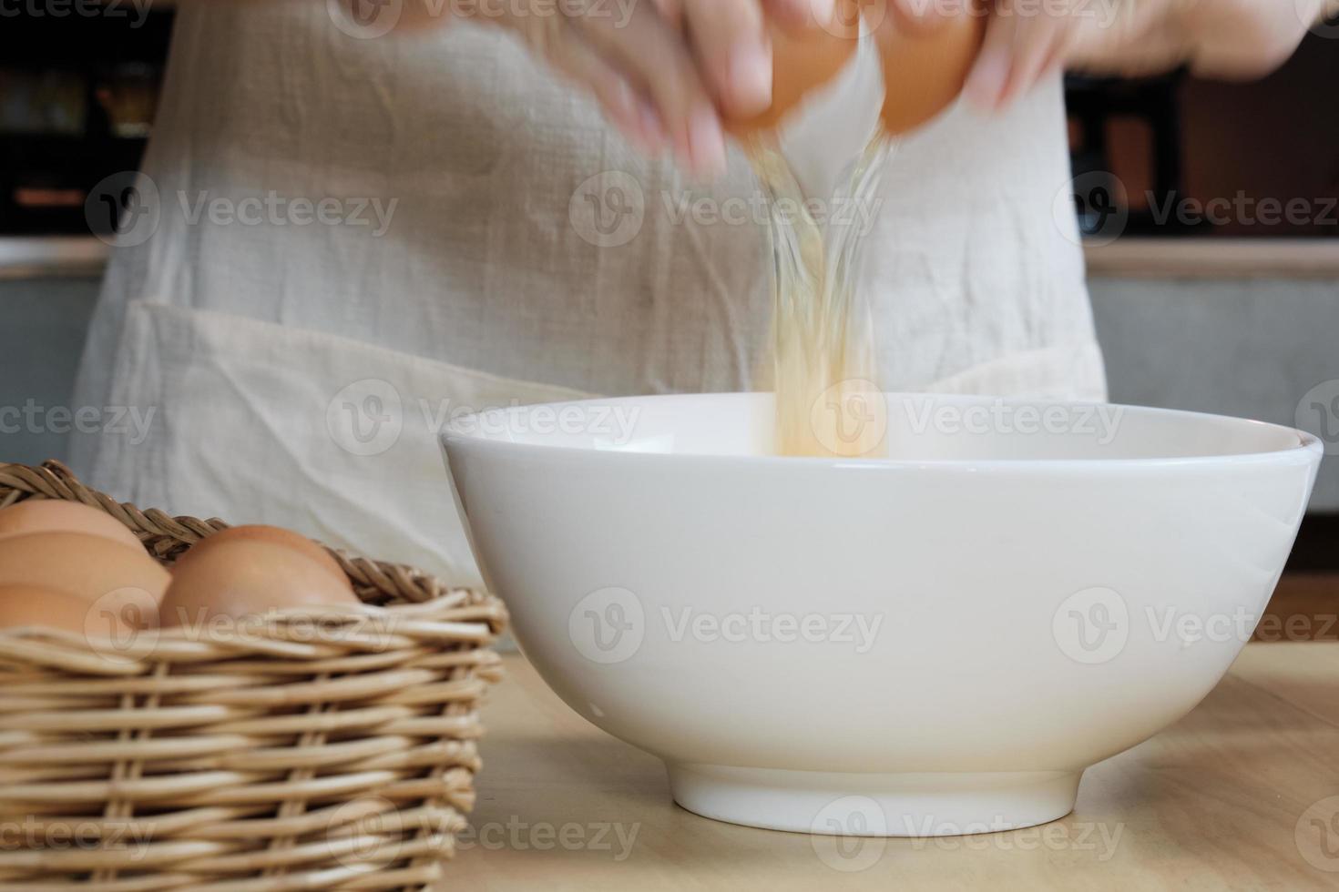 cuoca in un grembiule bianco sta rompendo un uovo nella cucina di casa. foto