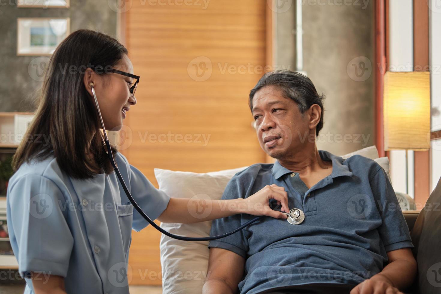 medico femminile che controlla la salute del paziente maschio anziano asiatico a casa. foto