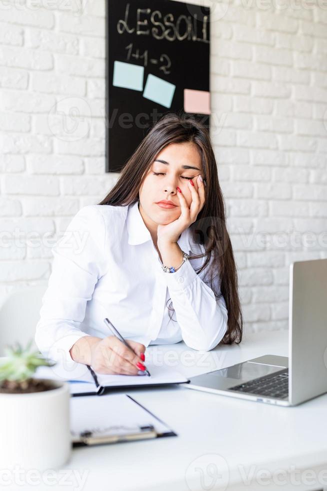 donna bruna triste o depressa che dorme al suo posto di lavoro foto