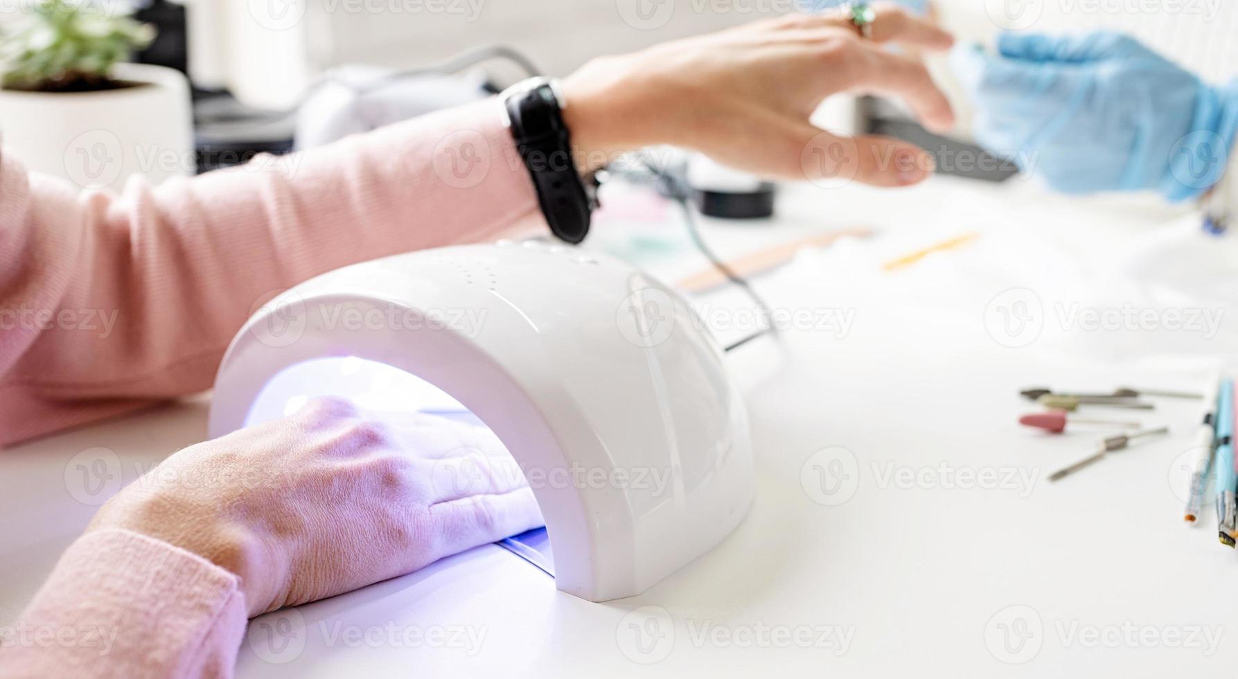 donna nel salone di manicure che si asciuga le unghie in una lampada uv foto