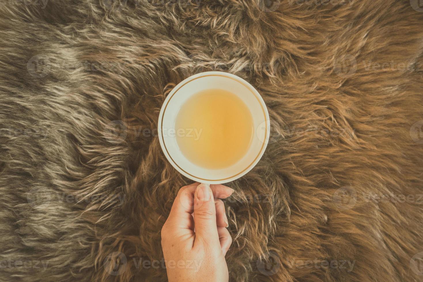 mano femminile che tiene una tazza di tè verde sul soffice plaid di pelliccia marrone. foto