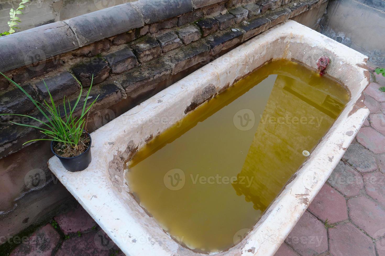 vasca da bagno rotta nel deserto con acqua sporca all'interno foto