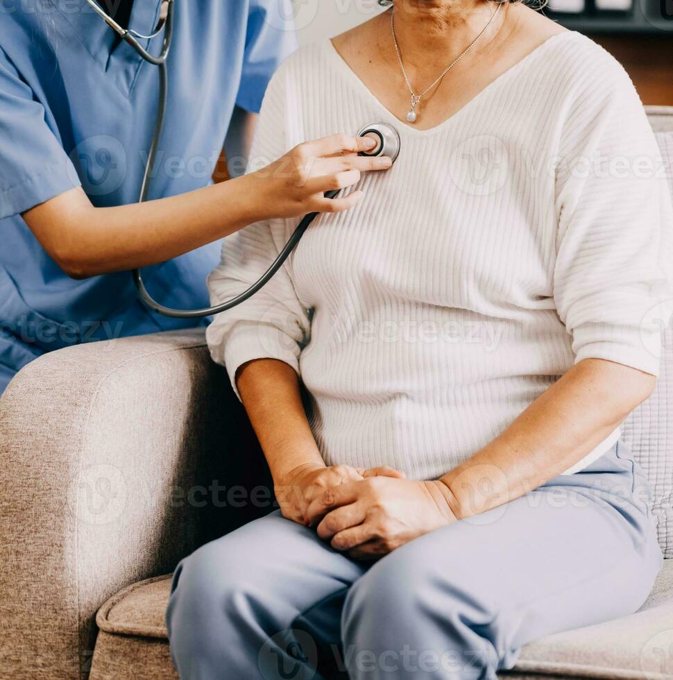 signora In arrivo per clinica per cuore e polmoni verifica, maschio medico utilizzando stetoscopio, ascoltando per femmina del paziente respiro o battito cardiaco, seduta nel clinica ufficio foto