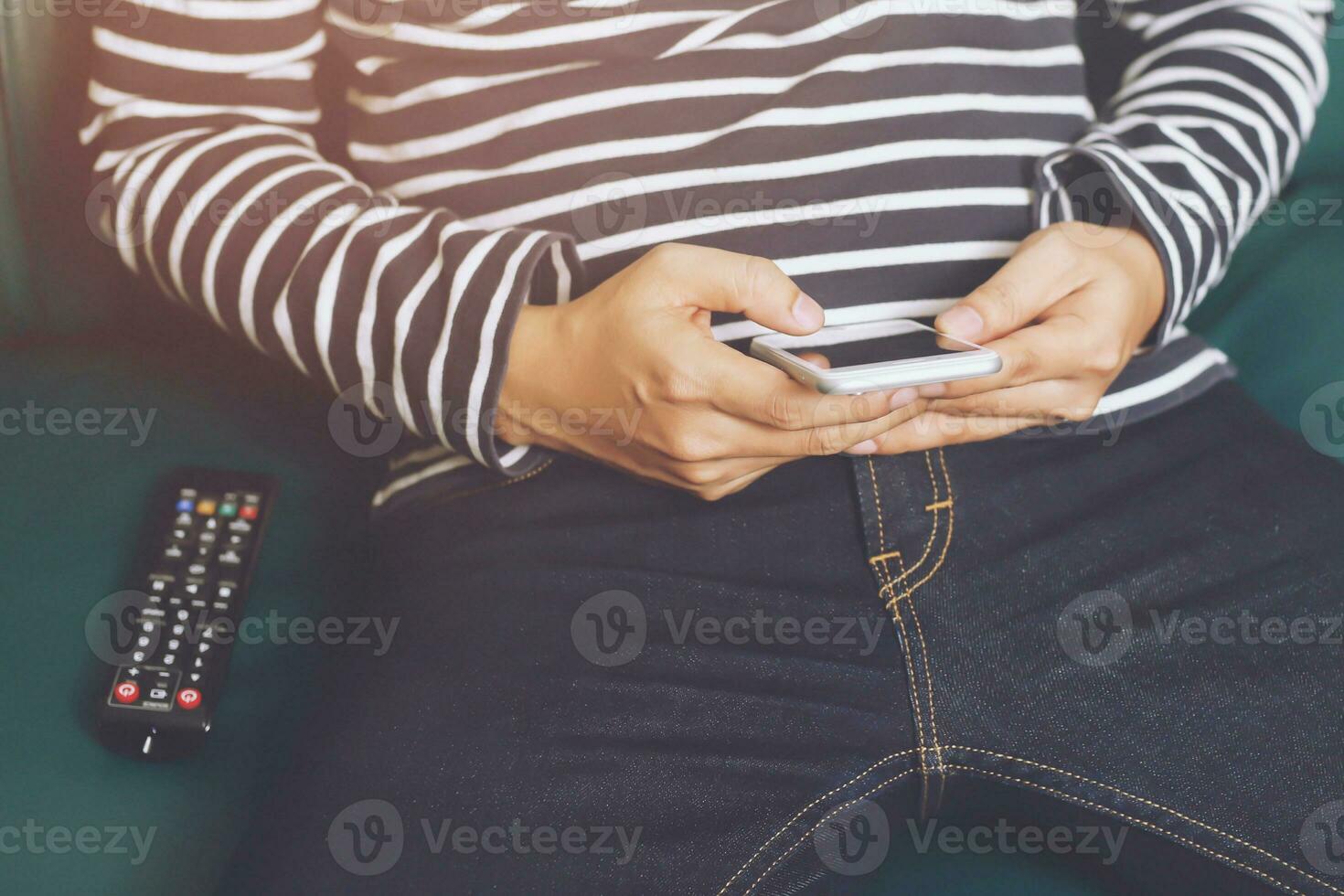 primo piano telecomando della televisione nelle mani dell'uomo casual che puntano al televisore e lo si accende o si spegne. seleziona il canale guardando la tv sul divano di casa in soggiorno rilassati. foto