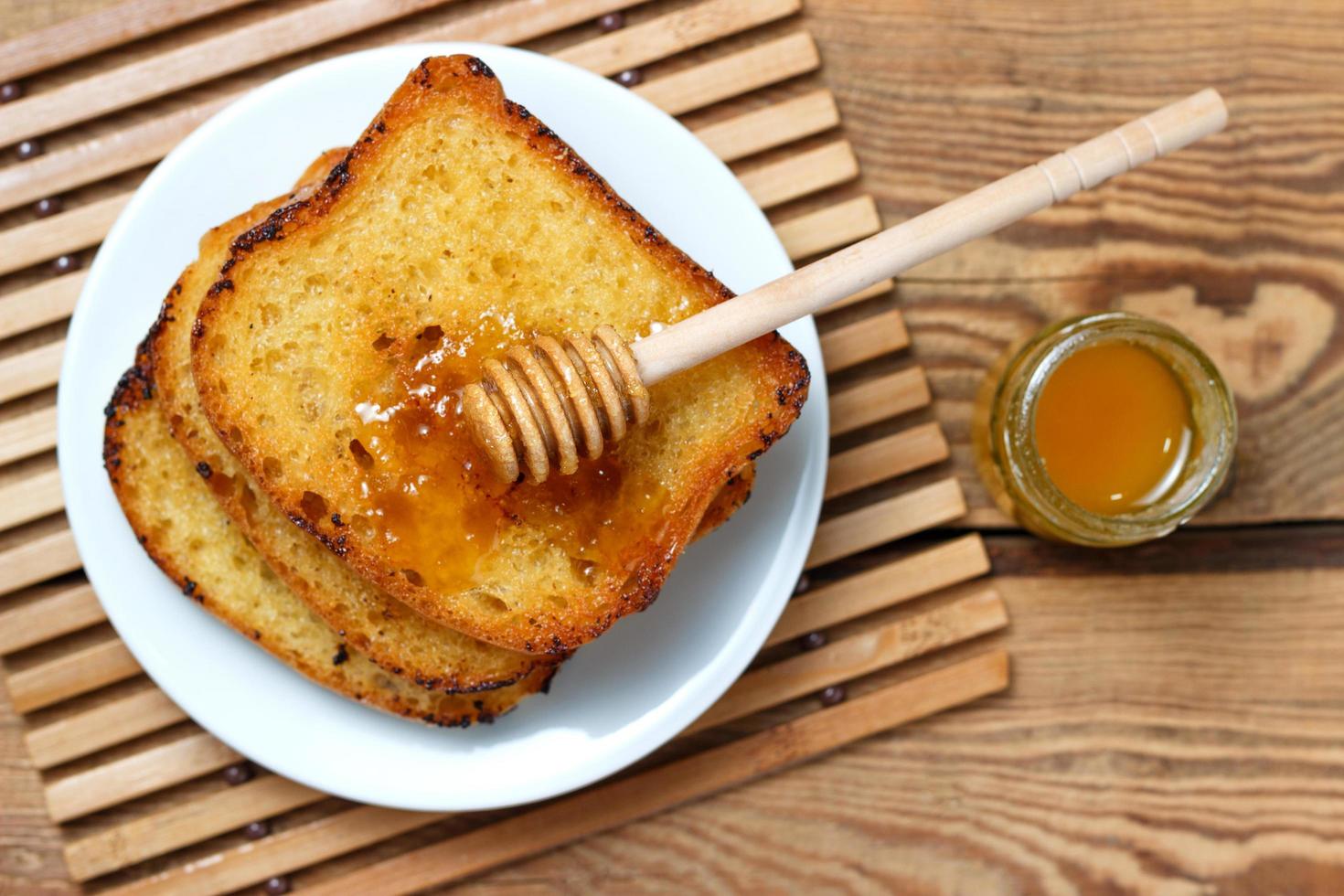 toast fritto su un piatto bianco con un vasetto di miele e un cucchiaio foto