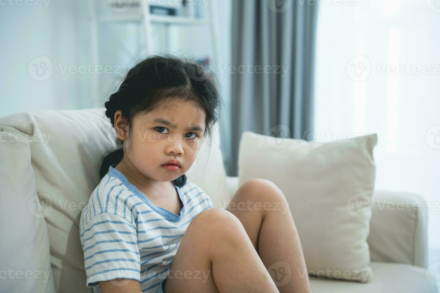 asiatico ragazzo ragazza irritato solitario Bullied poco guardare a telecamera si sente abbandonato abusato, triste solo seduta su il divano divano nel vivente camera a casa, beneficenza adozione concetto. foto