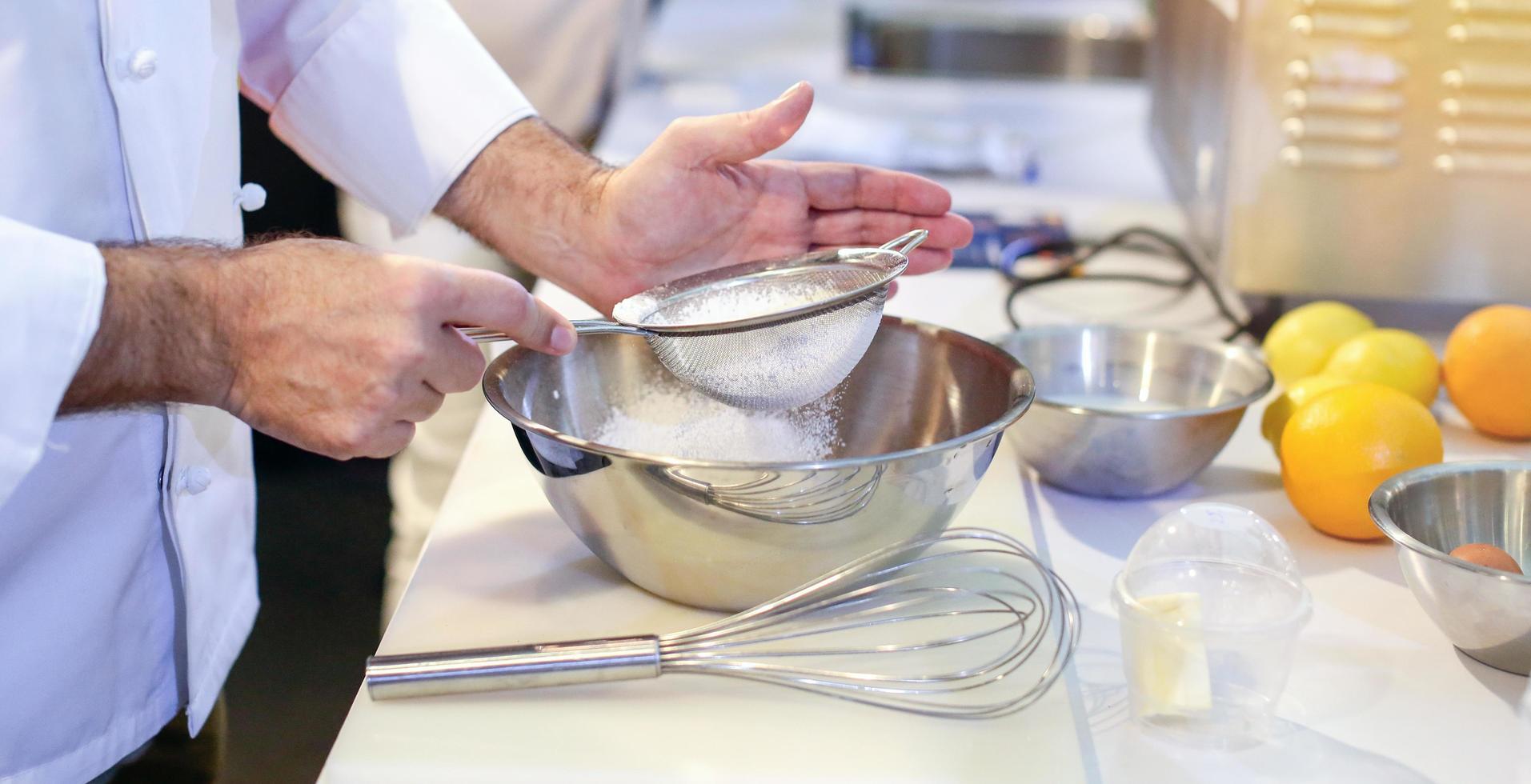 pasticcere fornaio setacciare la farina in una ciotola in cucina foto