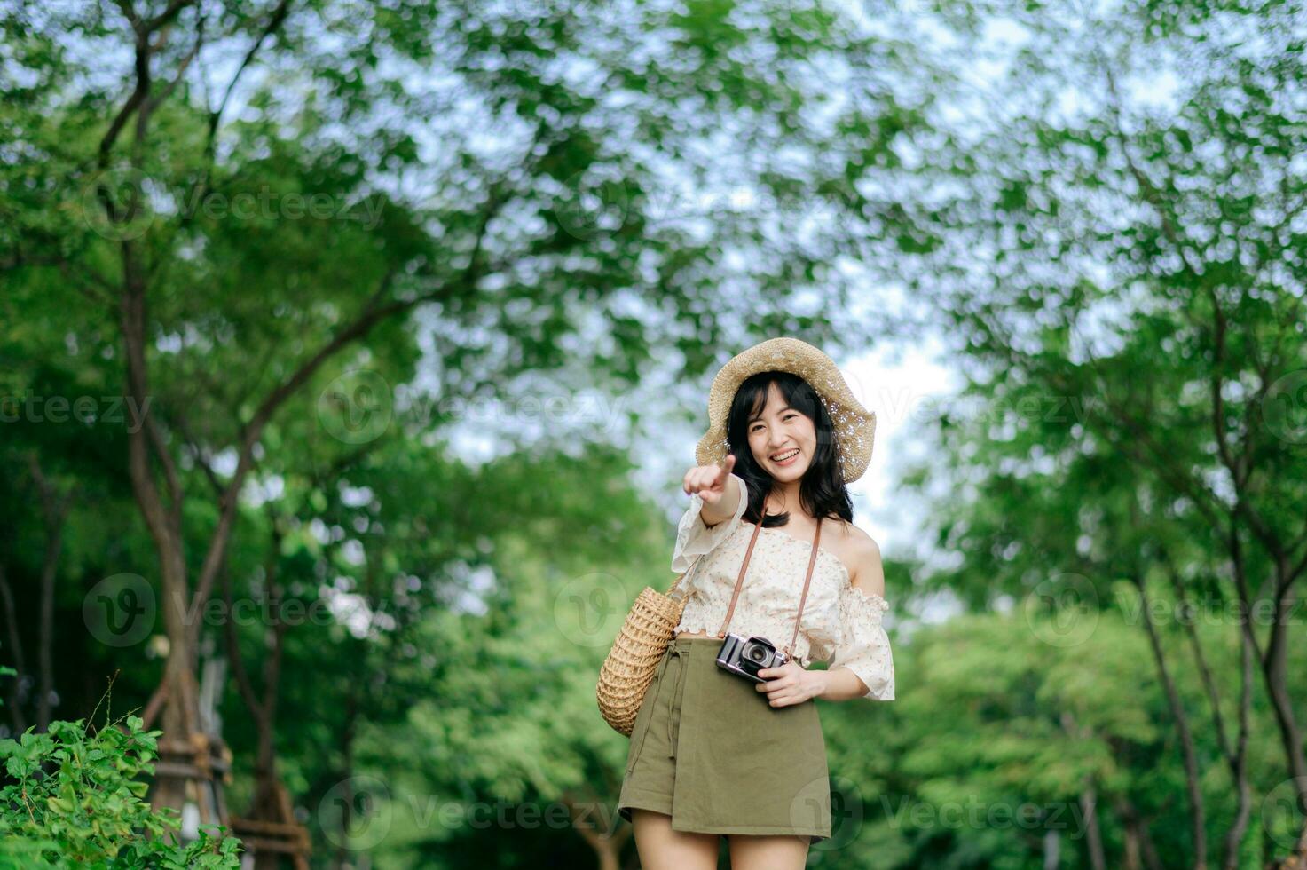 ritratto di asiatico giovane donna viaggiatore con tessitura cappello e cestino e un' telecamera su verde pubblico parco natura sfondo. viaggio viaggio stile di vita, mondo viaggio esploratore o Asia estate turismo concetto. foto