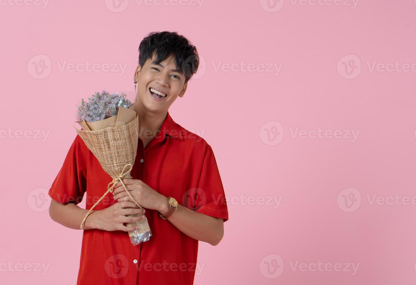 giovane uomo sorridente asiatico che tiene mazzo di fiori su sfondo rosa foto