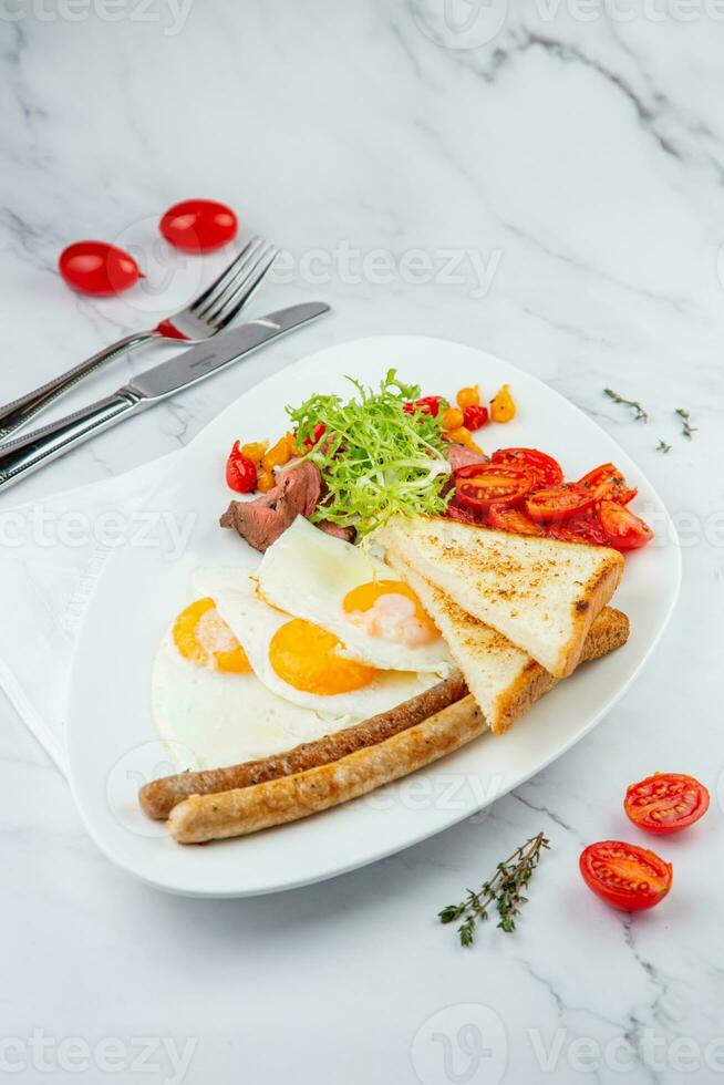 strapazzate uova con la verdura, ciliegia pomodori, pane, erbe aromatiche e salsicce su un' bianca piatto lato Visualizza foto