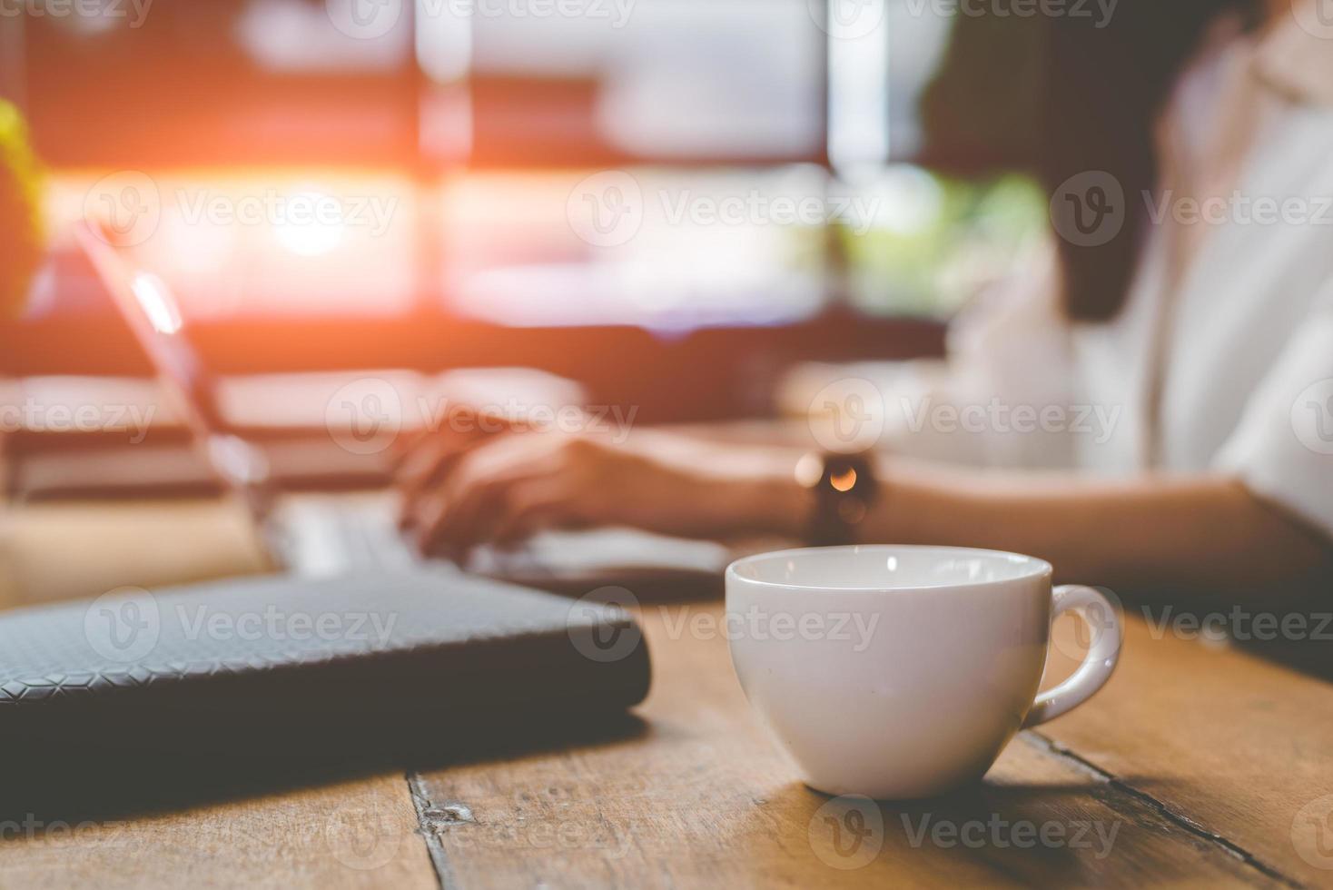 primo piano della tazza di caffè con una donna d'affari che lavora con il laptop foto