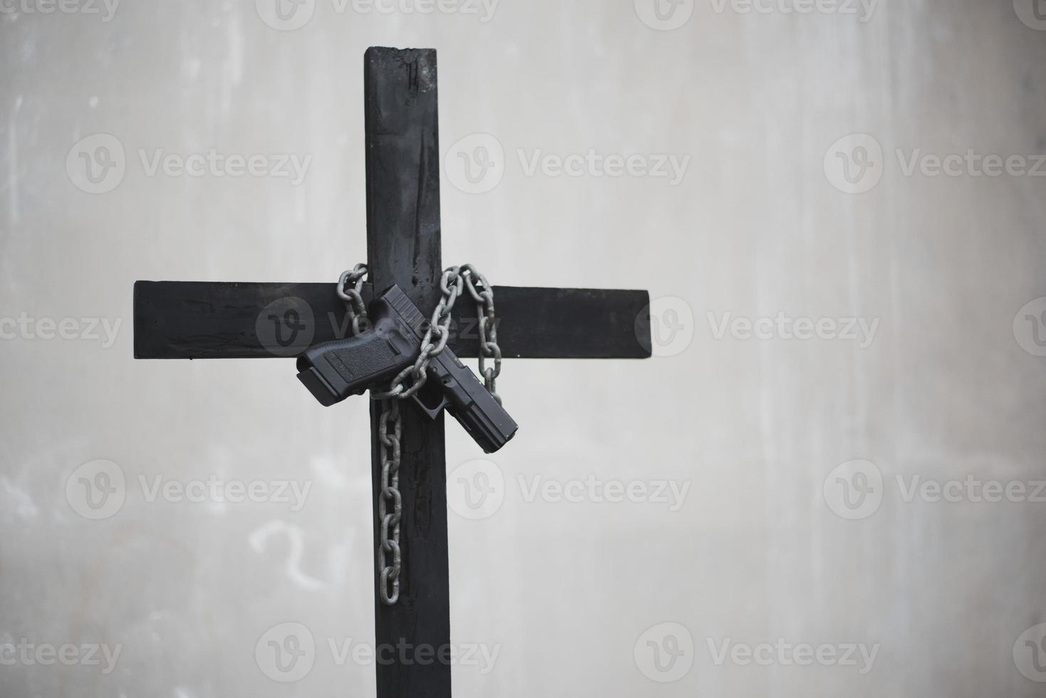 croce nera con catena e pistola su muro bianco grunge foto